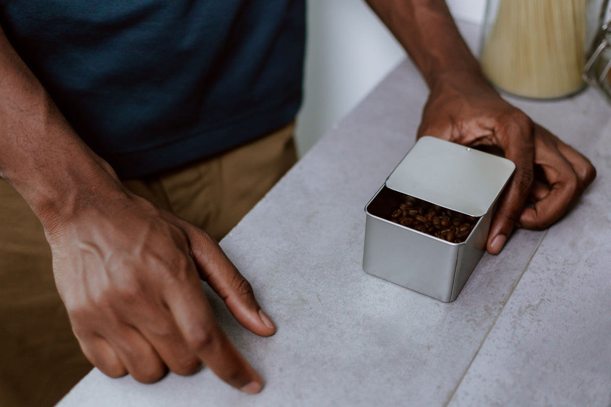 Person opening an opaque metal container filled with roasted coffee beans